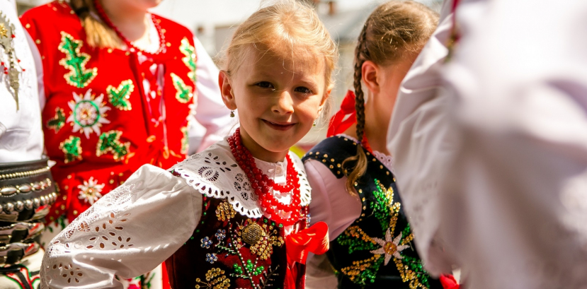 Mała dziewczyna w stroju ludowym idzie między większymi dziećmi ubranymi w stroje ludowe