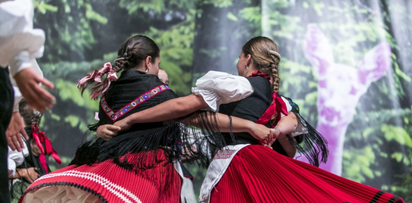 Dwie dziewczyny w czerwono czarnych strojach regionalnych tańczą obejmując się rękoma