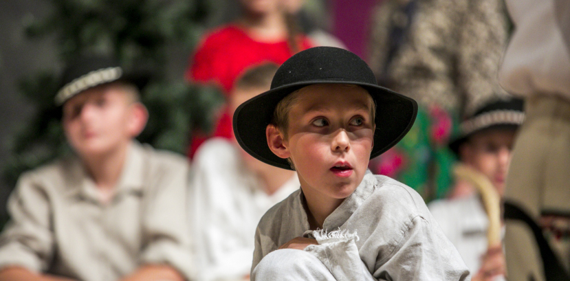 Chłopiec w góralskim kapeluszu kuca na scenie