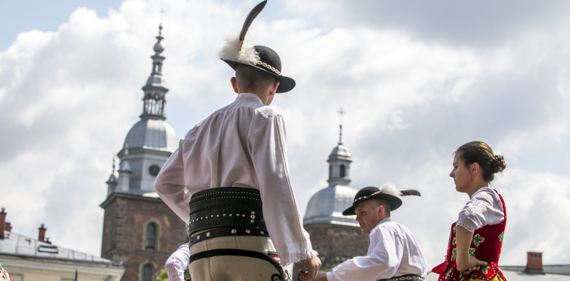Chłopiec w góralskim stroju stoi tyłem, na głowie ma kapelusz z piórem,  za nim widać niebo.