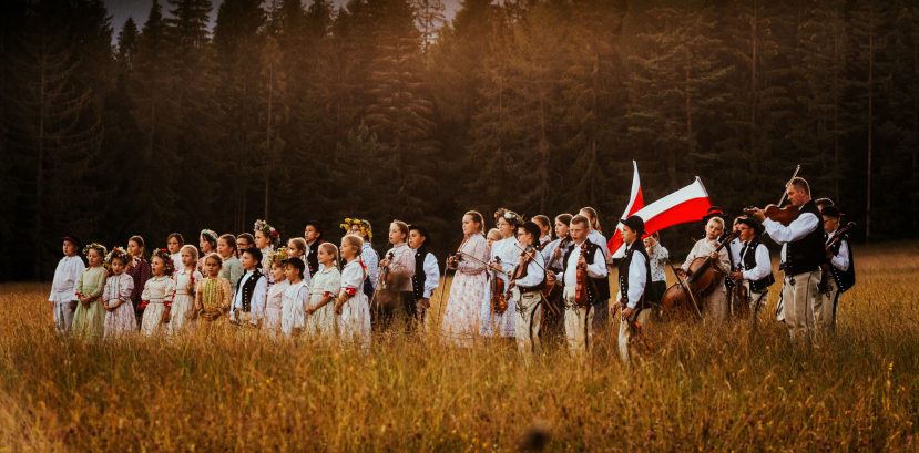 dzieci w strojach regionalnych pozują do zdjęcia na łące