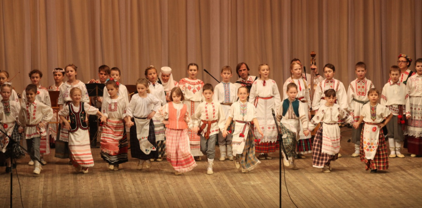 Dzieci w białoruskich strojach regionalnych trzymają się za ręce i tańczą na scenie