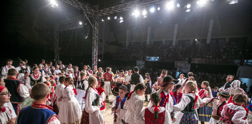duża liczba dzieci tańczy na scenie, w tle widać publikę, oświetlają ich reflektory