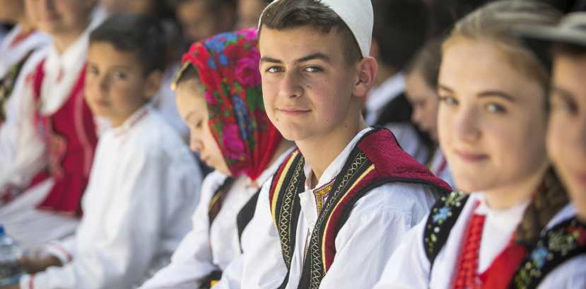 Dzieci w strojach regionalnych siedzą na ławkach