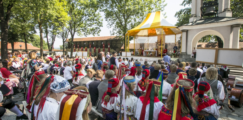 Ludzie siedzący na ławkach ustawionych na zewnątrz, w tle widać ołtarz