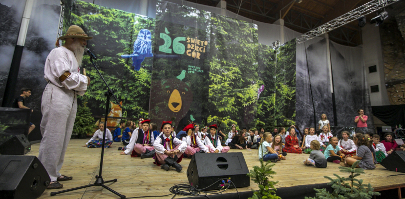 Dzieci siedzą na scenie, za nimi widać rysunek niedźwiadka