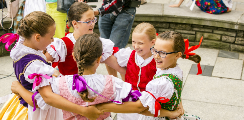 Dziewczynki w kolorowych strojach tańczą w kółeczku.