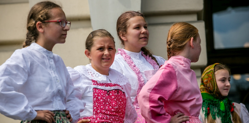 Dziewczynki w różowych strojach regionalnych stoją na płycie rynku.