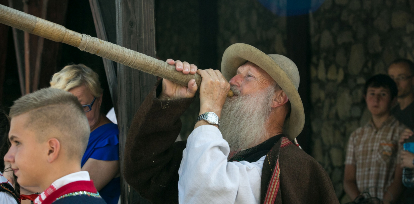 Mężczyzna z brodą gra na drewnianym instrumencie.