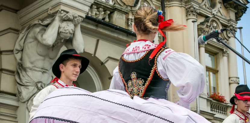 dziewczyna z warkoczem tańczy na scenie, za nią stoi chłopiec. oboje są w strojach regionalnych