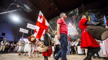 Ludzie w czerwonych strojach idą z flagą po scenie.