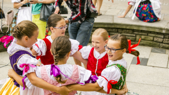 Dziewczynki w kolorowych strojach tańczą w kółeczku.