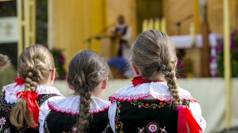 Dziewczynki siedzą odwrócone do ołtarza w strojach góralskich.