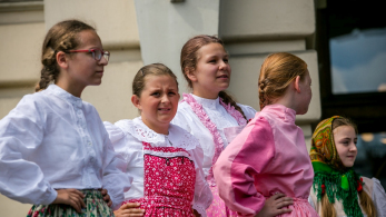 Dziewczynki w różowych strojach regionalnych stoją na płycie rynku.