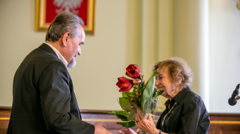 Mężczyzna podaje rękę i kwiatki starszej kobiecie.
