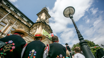 Chłopcy siedzą tyłem w strojach ludowych. W tle widać ratusz w Nowym Sączu.