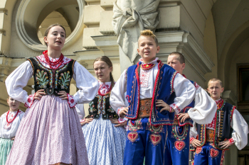 Dziewczyny i chłopcy w strojach ludowych stoją obok siebie. Wszyscy trzymają ręce w pasie.