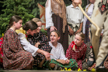 Dziewczynki w strojach ludowych siedzą na scenie.