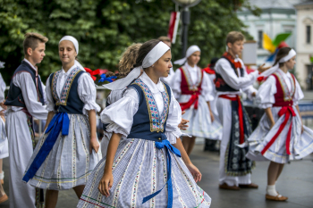 Młodzież w strojach ludowych tańczą na świeżym powietrzu.