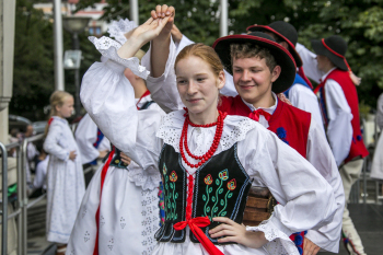 Dziewczyna i chłopak w strojach ludowych tańczą na scenie.