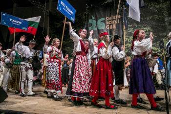 Młodzież w strojach ludowych na scenie. Niektórzy z nich trzymają tabliczki.