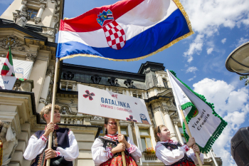 Dzieci w strojach ludowych stojące z flagą i tabliczką.