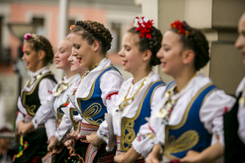 Grupa kobiet w strojach ludowych, w spiętych włosach tańczą ze soba.