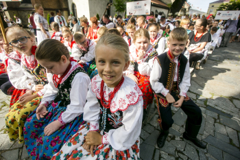 Dzieci w strojach góralskich siedzą na ławkach przy kościele.