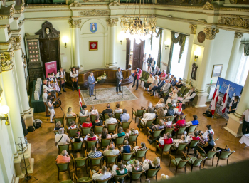 Ludzie siedzą na krzesłach tyłem do zdjęcia.