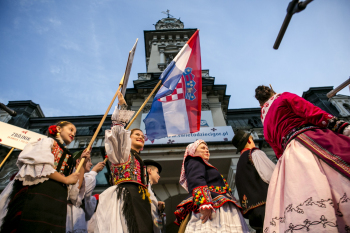 Dziewczyny w strojach ludowych trzymają flagę.