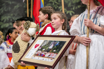 Dziewczynka w stroju ludowym trzyma duże zdjęcie w ramie.