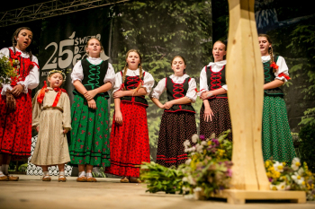 Grupa dziewczyn w strojach ludowych stoi na scenie.