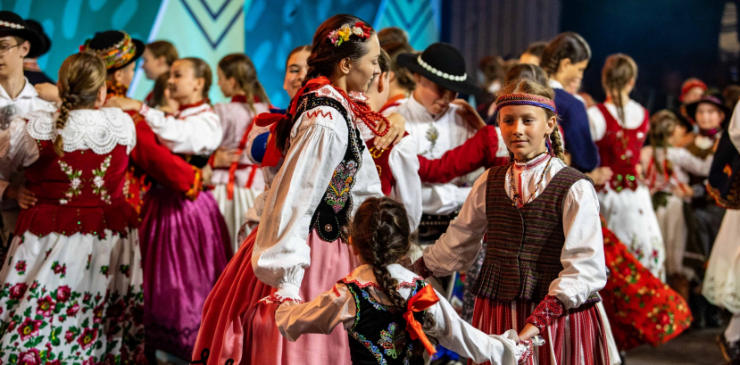 Dzieci w regionalnych strojach stoją na scenie, w tle widać plac z publicznością